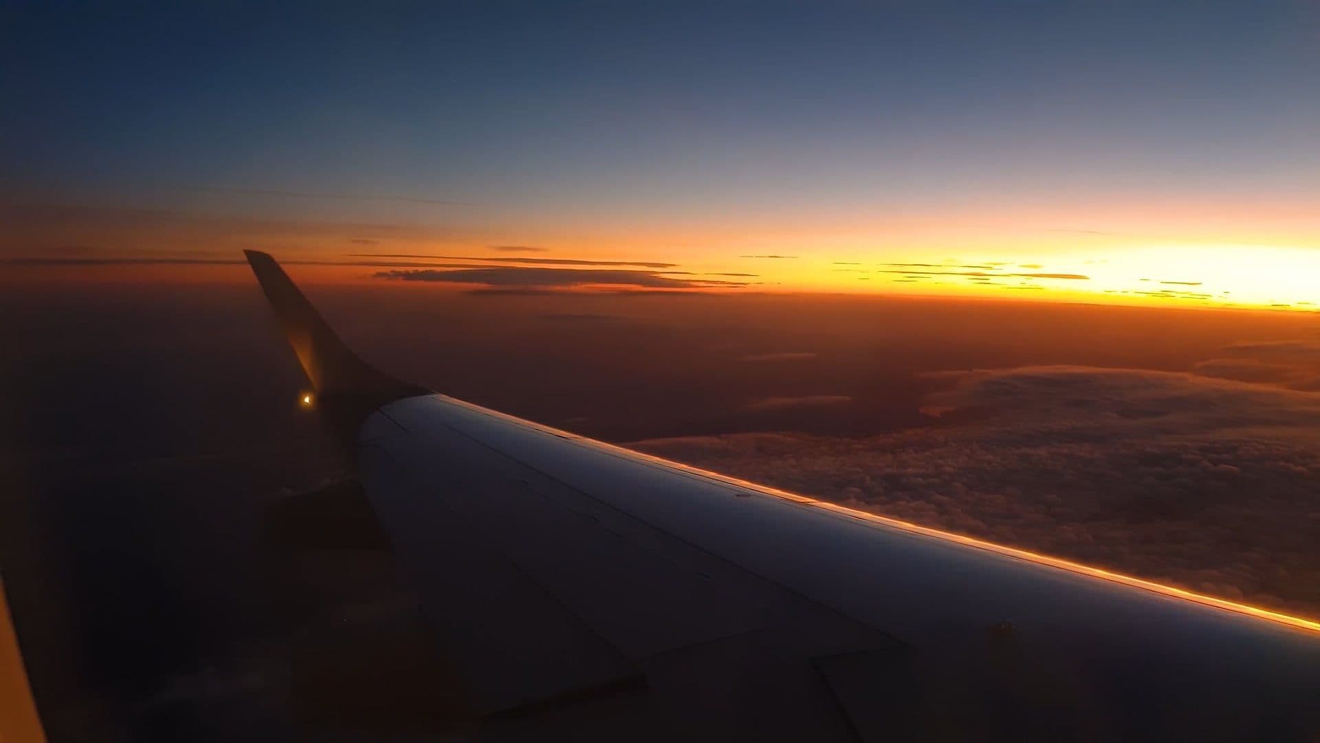 View of a private jet wing flying above the clouds at sunset, luxury aviation atmosphere